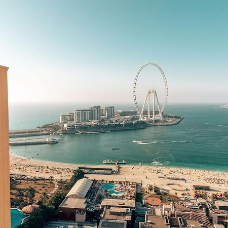 Amwaj Rotana, Jumeirah Beach - Dubai Esterno foto The photo shows a stunning coastal view featuring a large Ferris wheel, likely situated on an island or seaside area. In the foreground, there is a high-rise building with a distinctive logo, while below, you can see a beach with umbrellas and people