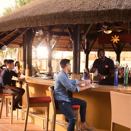 Amwaj Rotana, Jumeirah Beach - Dubai Esterno foto The photo shows a bar area with a thatched roof. There are several people seated at the bar. On the left, two individuals are chatting together, while a bartender is serving a customer in the foreground. The customer is wearing a blue shirt and sitti