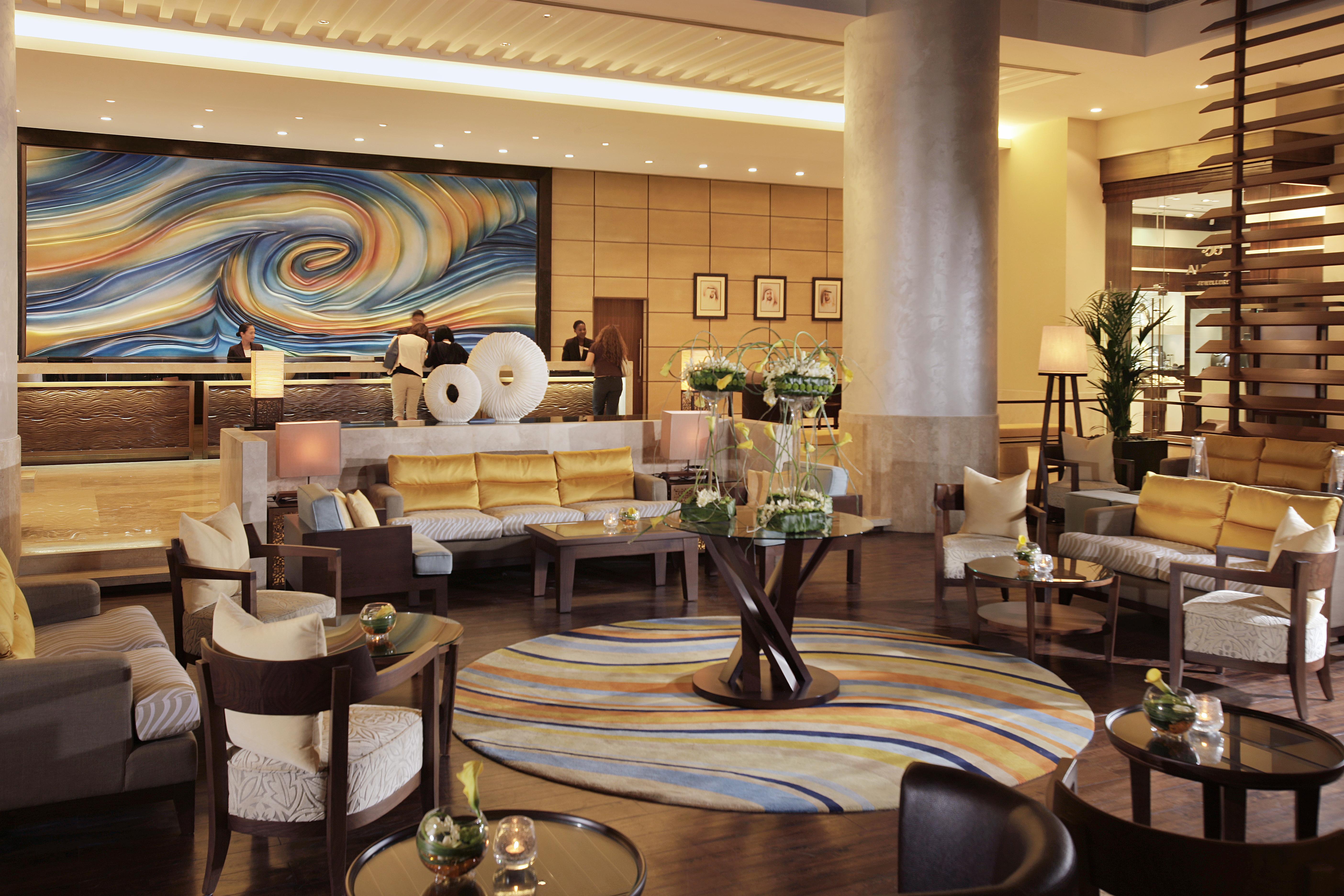 Amwaj Rotana, Jumeirah Beach - Dubai Interno foto The photo shows a stylish and contemporary hotel lobby. It features a spacious seating area with comfortable sofas and armchairs arranged around coffee tables. The decor includes a large, vibrant mural with swirling colors on one wall, adding an arti