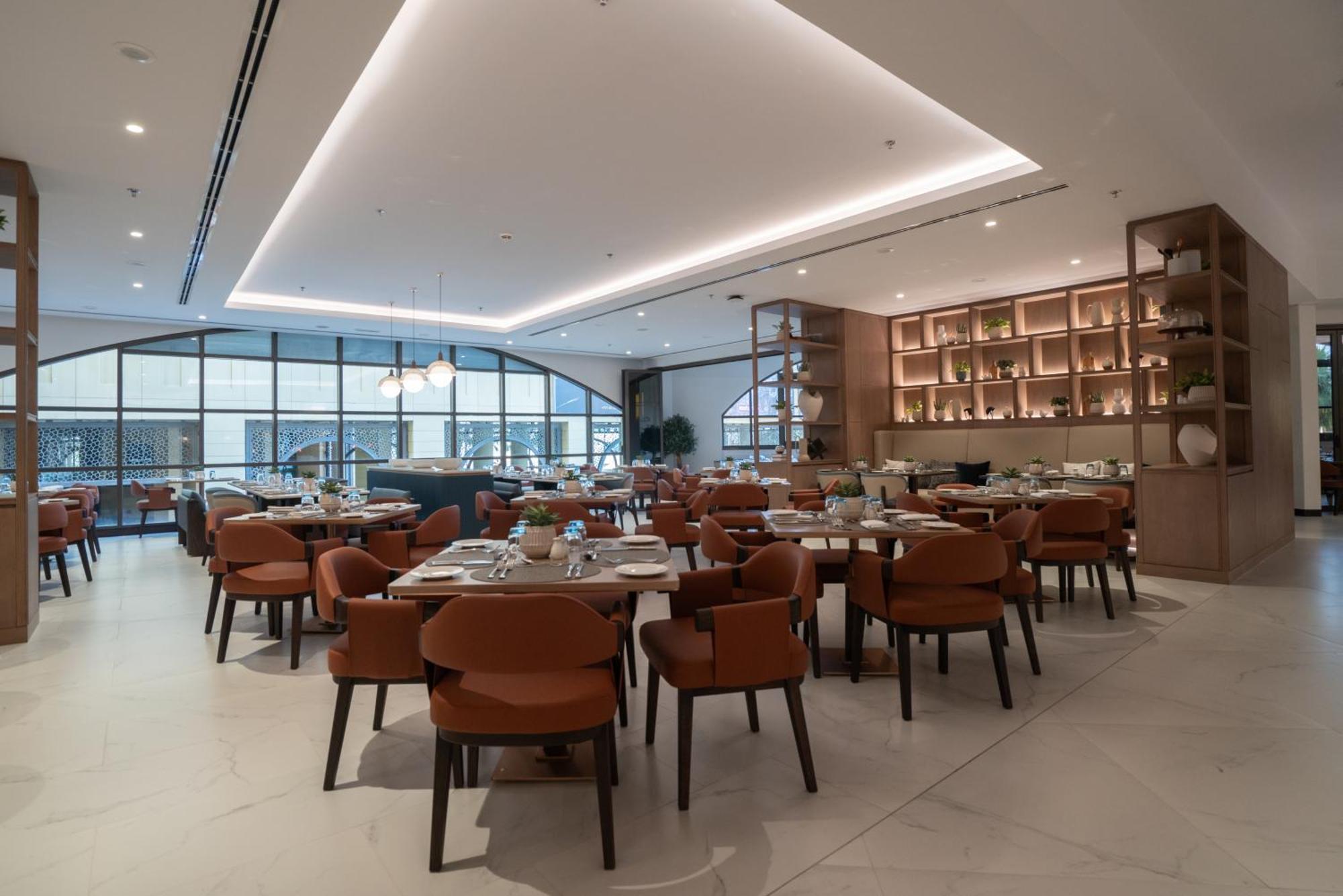 Amwaj Rotana, Jumeirah Beach - Dubai Esterno foto The photo shows a modern restaurant interior. It features a spacious dining area with neatly arranged tables and stylish chairs. The color scheme includes warm tones, with brown chairs and light-colored surfaces. The ceiling has a sleek design with s