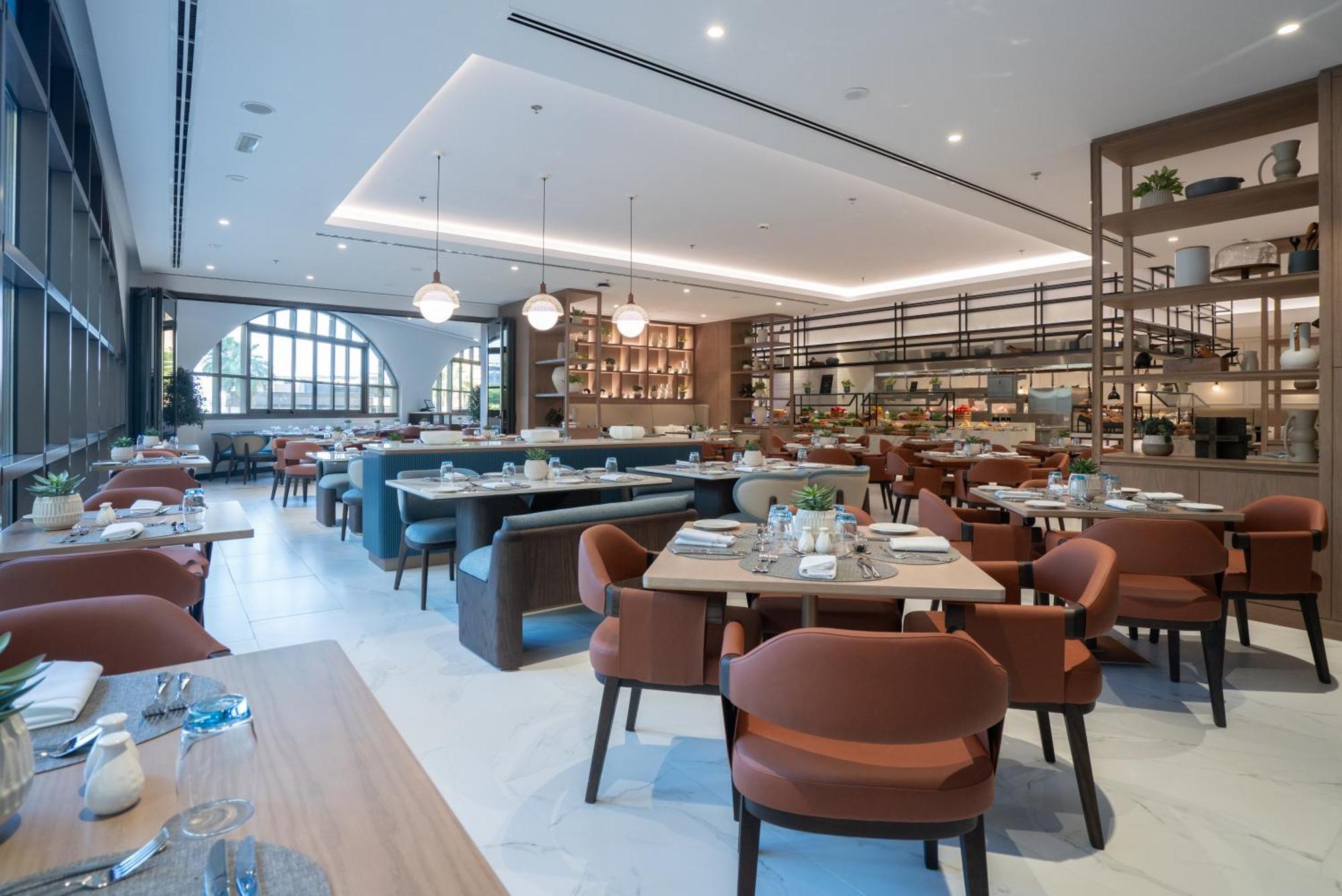 Amwaj Rotana, Jumeirah Beach - Dubai Esterno foto The photo depicts a modern restaurant interior. It features an open dining area with a mix of tables and comfortable, rounded chairs in muted colors. The decor is sleek and contemporary, with soft lighting provided by pendant lamps. Large windows all