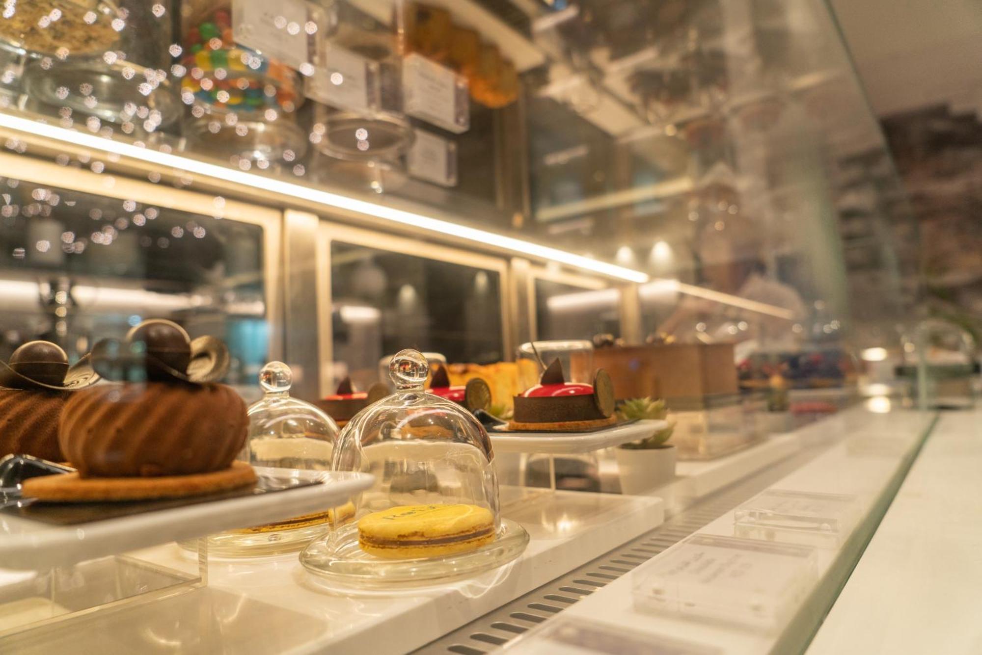 Amwaj Rotana, Jumeirah Beach - Dubai Esterno foto The photo shows a display case featuring a variety of desserts. Each dessert is presented under a small glass dome, showcasing their intricate designs. The treats include a round chocolate pastry, a small cake topped with colorful fruits, and a yello