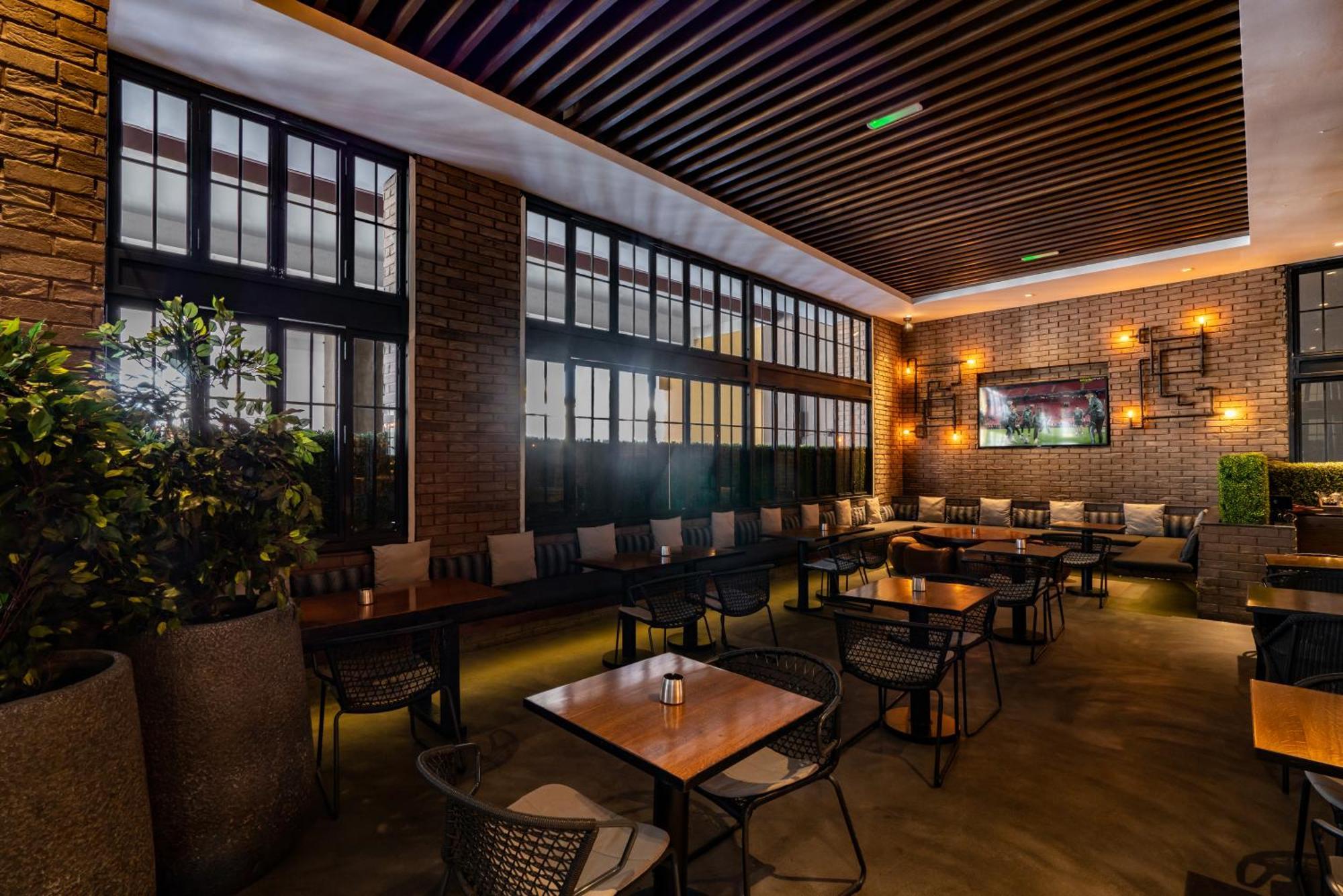 Amwaj Rotana, Jumeirah Beach - Dubai Esterno foto The photo shows a modern interior of a restaurant or café. It features a spacious area with large windows allowing natural light to enter. The walls are a combination of brick and wood, creating a warm atmosphere. There are several tables with chairs